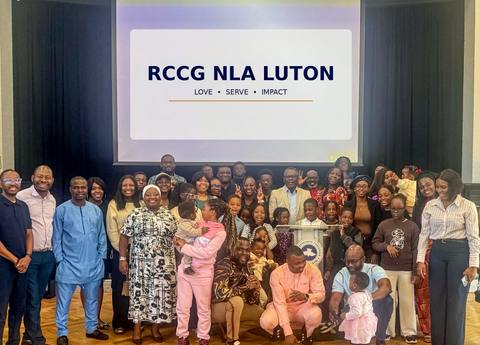 The RCCG New Life Assembly church family together in front of a screen reading RCCG NLA Luton: Love, Serve, Impact